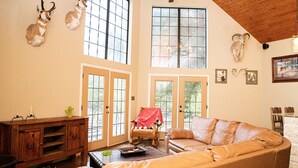 A spacious living room with a leather sofa, a wooden cabinet, and mounted animal heads on the wall. - ANTLER OAKS CABIN  (San Saba)