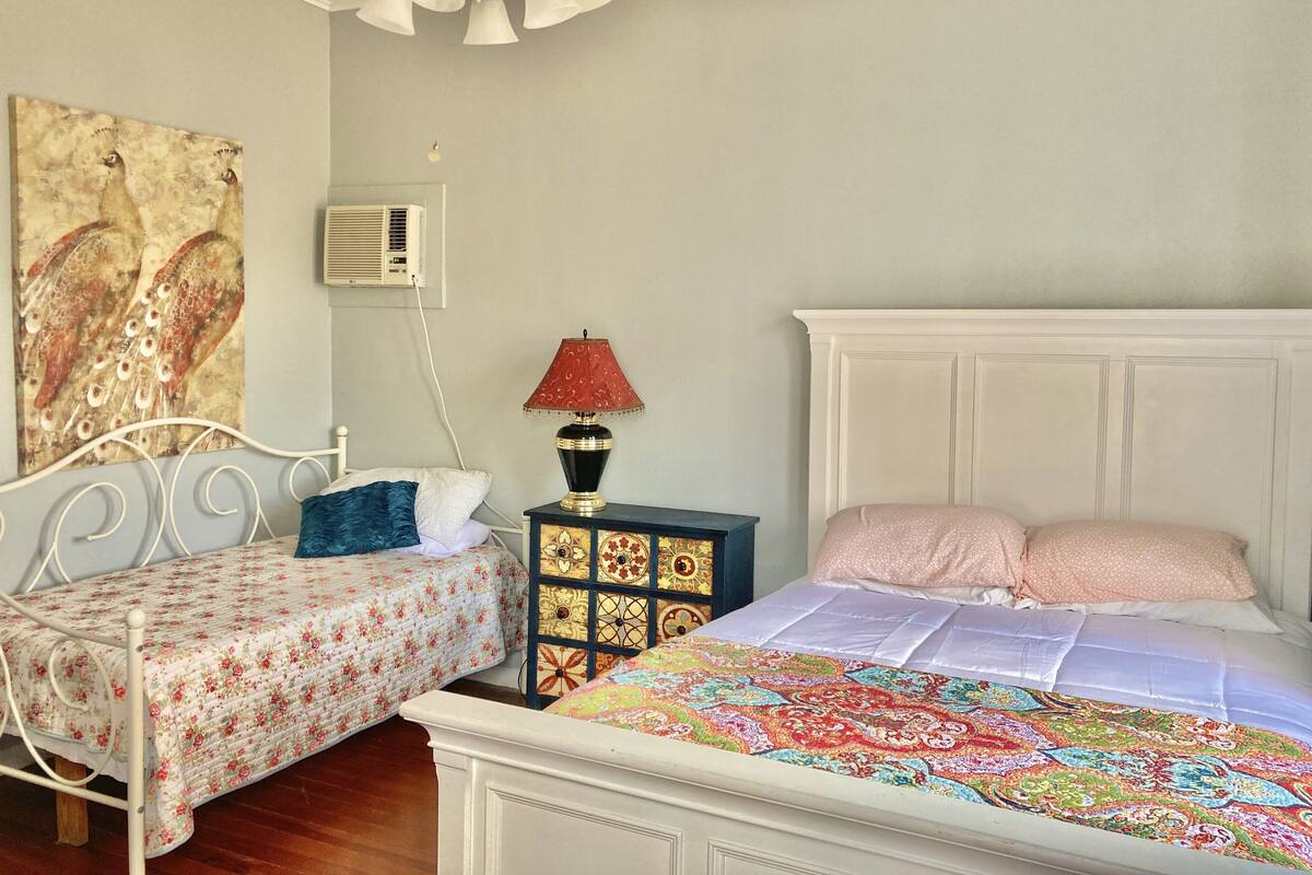 Un dormitorio con dos camas individuales, un ventilador de techo, un aire acondicionado de pared y una lámpara decorativa.