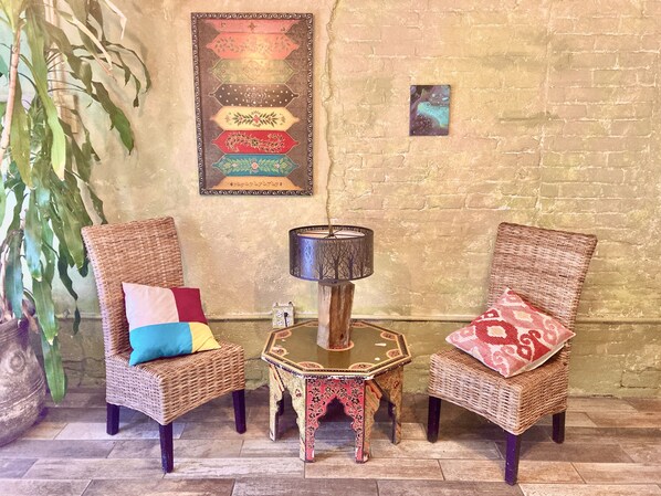 Une pièce comprenant deux fauteuils en osier, une petite table avec une lampe et une grande plante en pot.