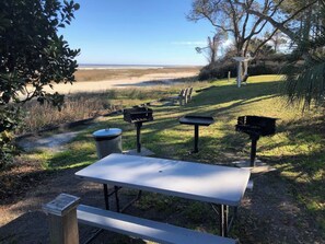 An outdoor seating area with a table and benches, a trash bin, and a view of the beach. - Beachside Bliss Villa with Pools & Tennis (Hilton Head Island)