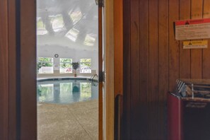 An indoor swimming pool with a wooden wall, windows, and a caution sign.