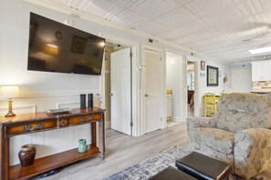 A living room with a flat-screen TV, a wooden console table, a patterned armchair, and a door leading to another room.