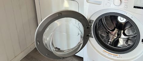 Ein Waschbereich mit Waschmaschine, Trockner und einem darüberliegenden Ablagefach mit einer Waschmittelflasche.