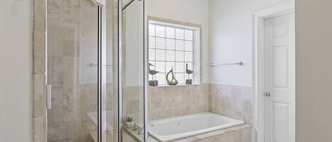 Un baño con cabina de ducha de vidrio, bañera y ventana con adornos.