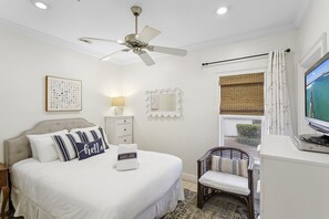 Ein Schlafzimmer mit Bett, Stuhl, Schreibtisch, Fernseher und Deckenventilator.