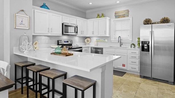 Una cocina moderna con armarios blancos, una isla central con taburetes, electrodomésticos de acero inoxidable y detalles decorativos.