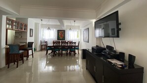 A spacious living room with a dining area, a flat-screen TV mounted on the wall, and a black entertainment unit. - Comfortable, spacious and beautiful apartment (Santo Domingo)