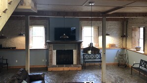 Ein großzügiges Loft mit Steinfußboden, Kamin, Fernseher und einem großen Fenster.