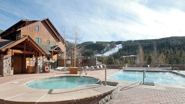 A pool area with two hot tubs, a wooden building, and a mountainous backdrop. - River Run Village Walk To Gondola Pool and Hot Tubs Restaurants and Shops (Keystone)