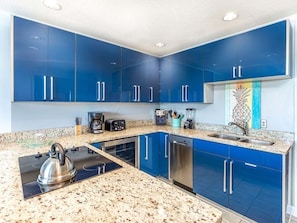 Une cuisine moderne avec des meubles bleus, un plan de travail en granit, une bouilloire, une machine à café et un lave-vaisselle.