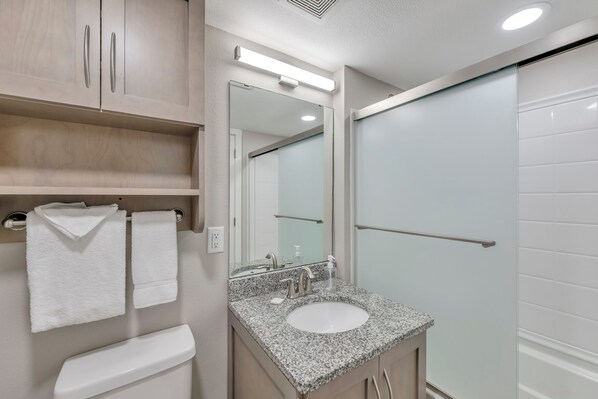 Une salle de bain moderne avec un lavabo en granit, des accessoires blancs et une cabine de douche en verre.