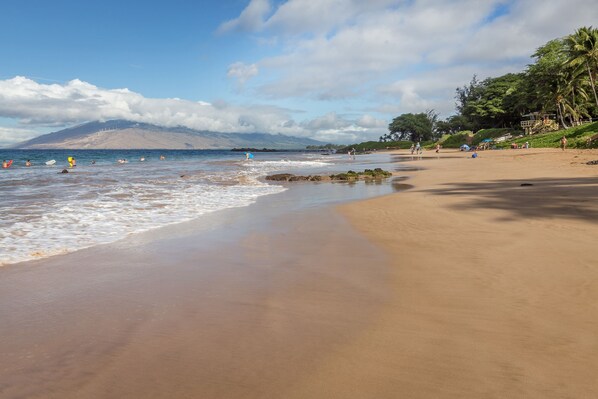 Une plage avec un ciel dégagé, une eau calme et une montagne qui se profile à l’horizon.