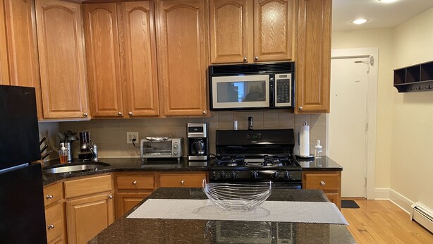 A kitchen with wooden cabinets, a microwave, a toaster, a coffee maker, and a stove. - Charming 2nd Floor Haven (Westfield)