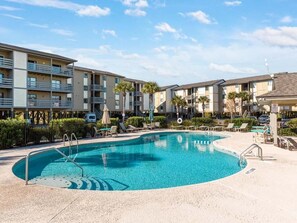 A swimming pool surrounded by a multi-story building with balconies, a lifeguard stand, and lounge chairs.