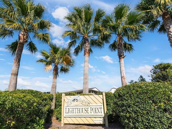 A sign for Lighthouse Point with palm trees and a clear sky.