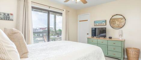 A bedroom with a bed, a ceiling fan, a window, a dresser, and a wall-mounted TV.