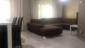 Un salon avec un canapé marron, une table à manger avec des chaises et une petite table d’appoint blanche.