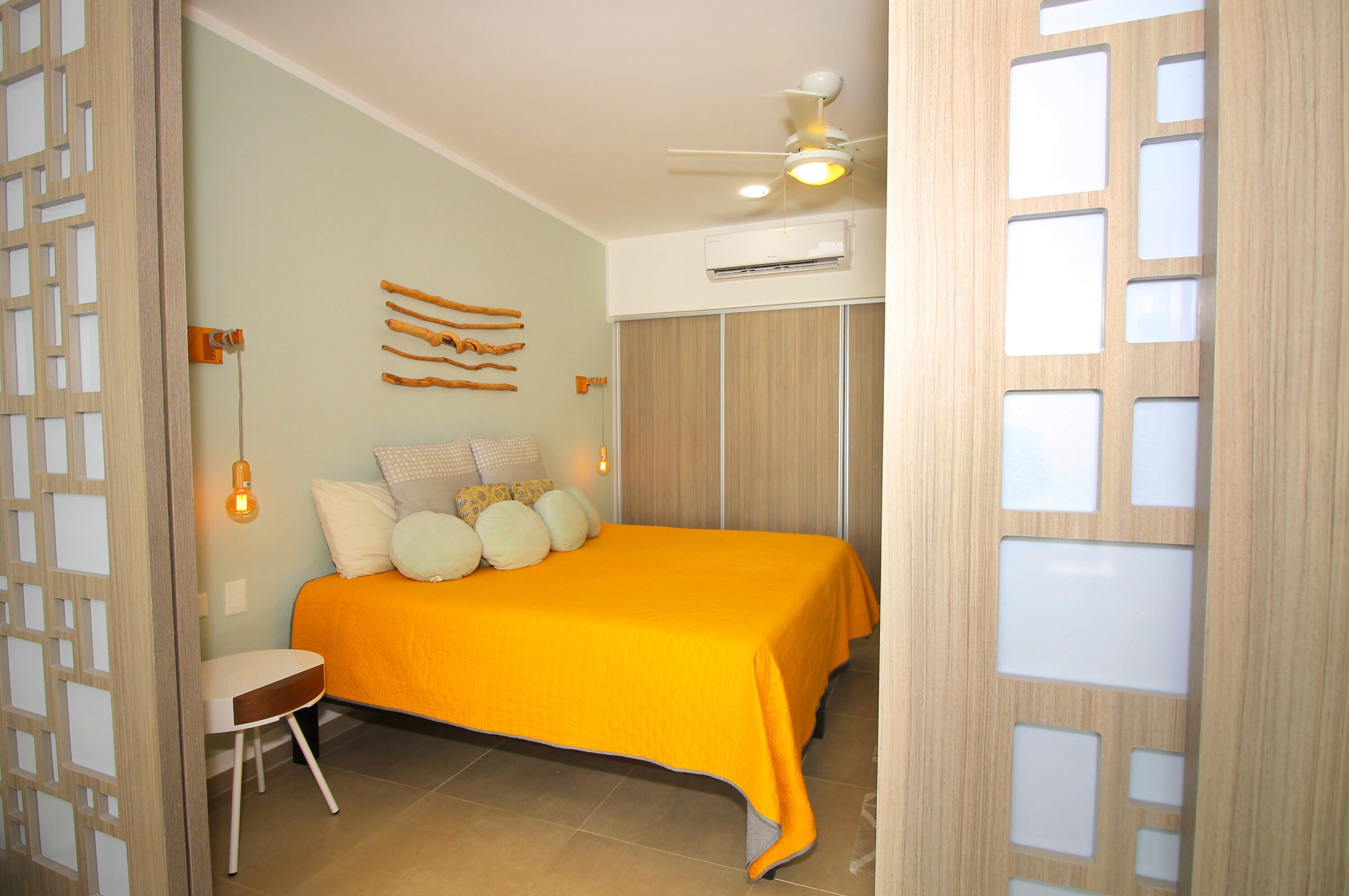 A bedroom with a bed, a chair, a ceiling fan, and a wall-mounted air conditioner.
