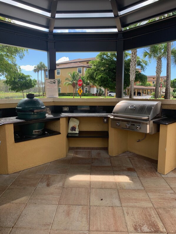 A covered outdoor kitchen area with a grill, a bag of charcoal, and a stop sign in the background. - Luxurious Lake Front Condo 2/2, First Floor Unit (Naples)