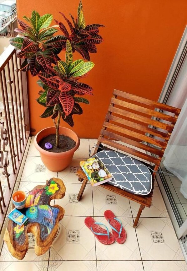 A balcony with a wooden chair, a potted plant, a small stool, and a pair of flip-flops. - Boutique Hotel Casa de Lis (Turrialba)