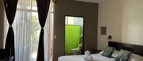 A hotel room with a bed, curtains, a ceiling fan, and a view of the outside.