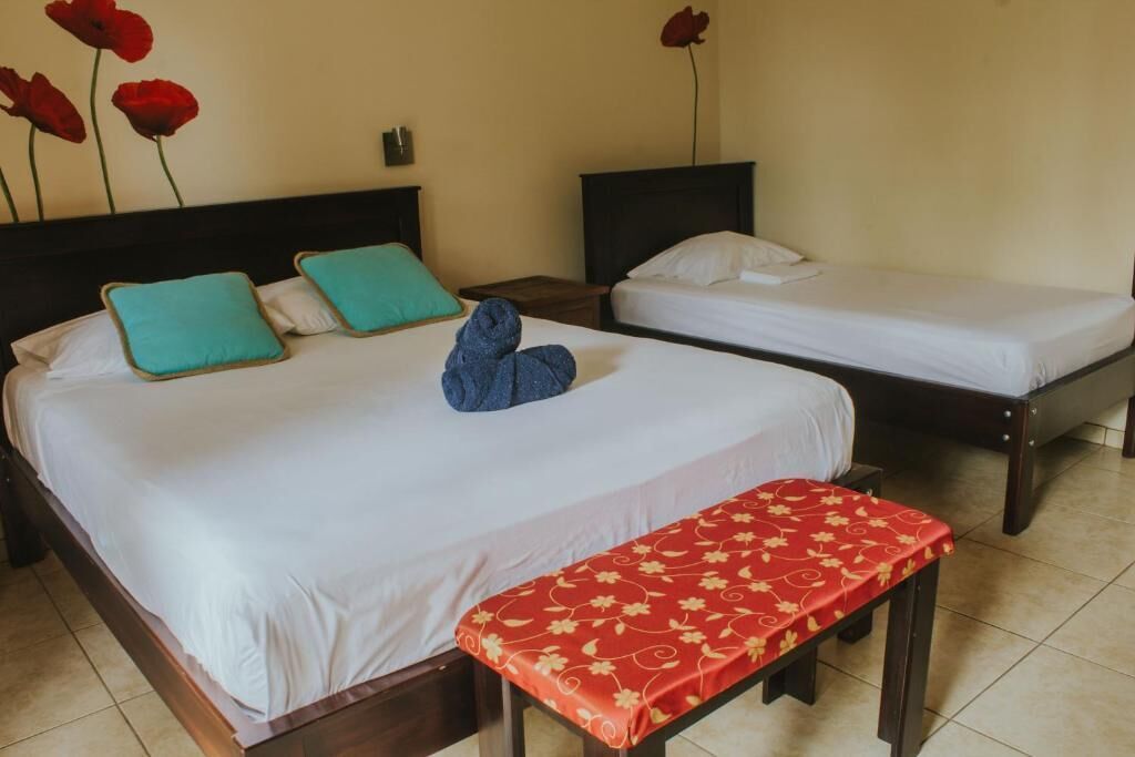 A hotel room with two single beds, a bench, and a wall with red flowers.