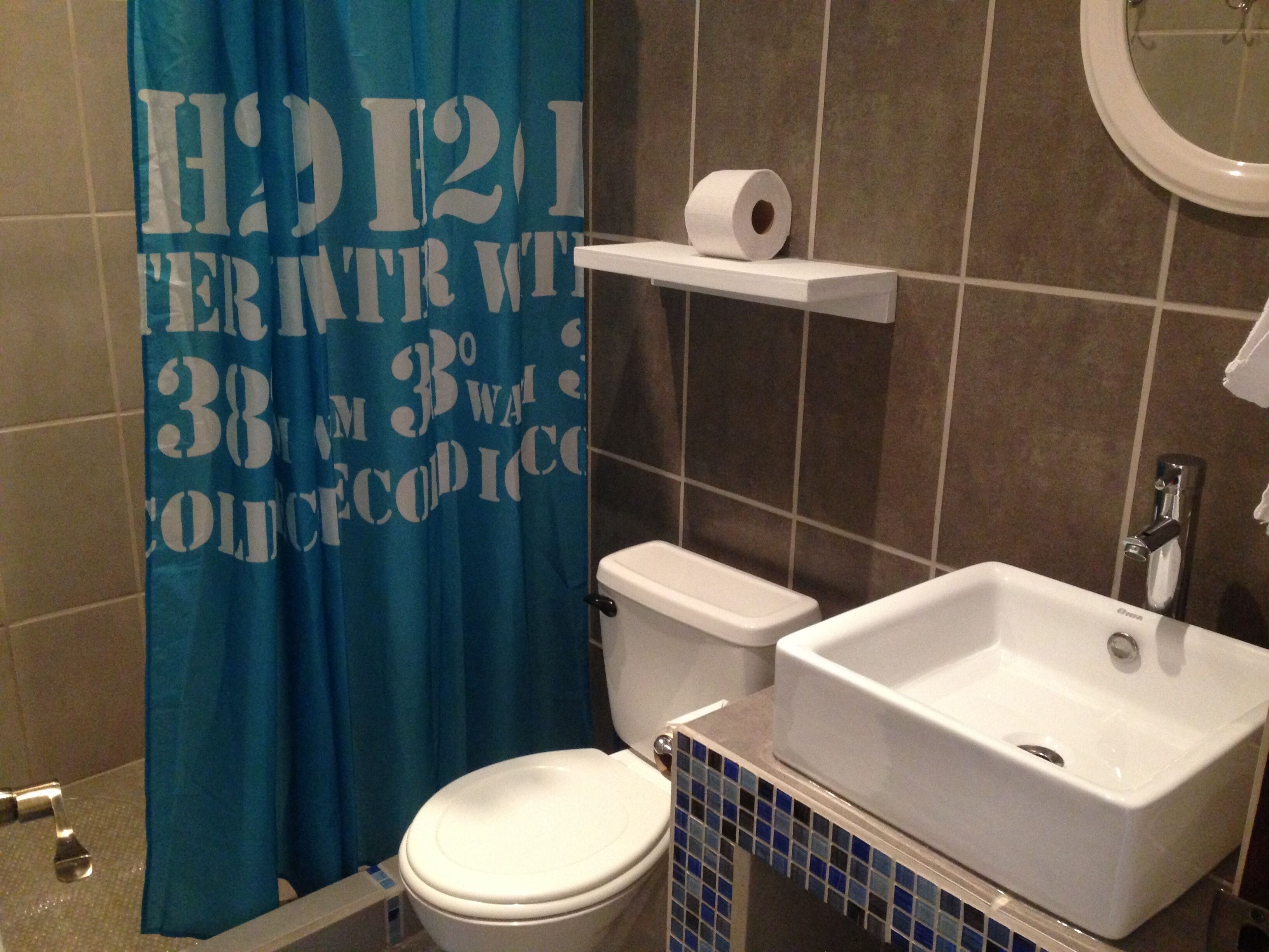 Une salle de bain équipée de toilettes, d’un lavabo et d’un rideau de douche orné de motifs ou d’inscriptions.