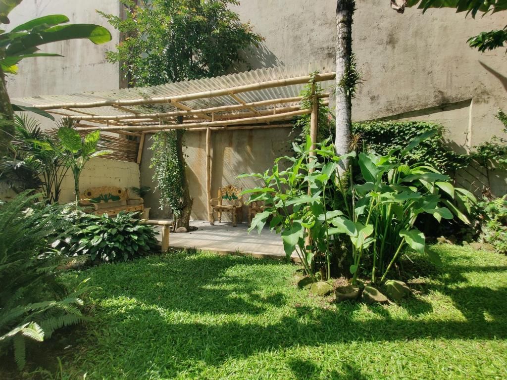 A covered outdoor seating area with a bamboo structure, surrounded by lush greenery and a concrete wall.