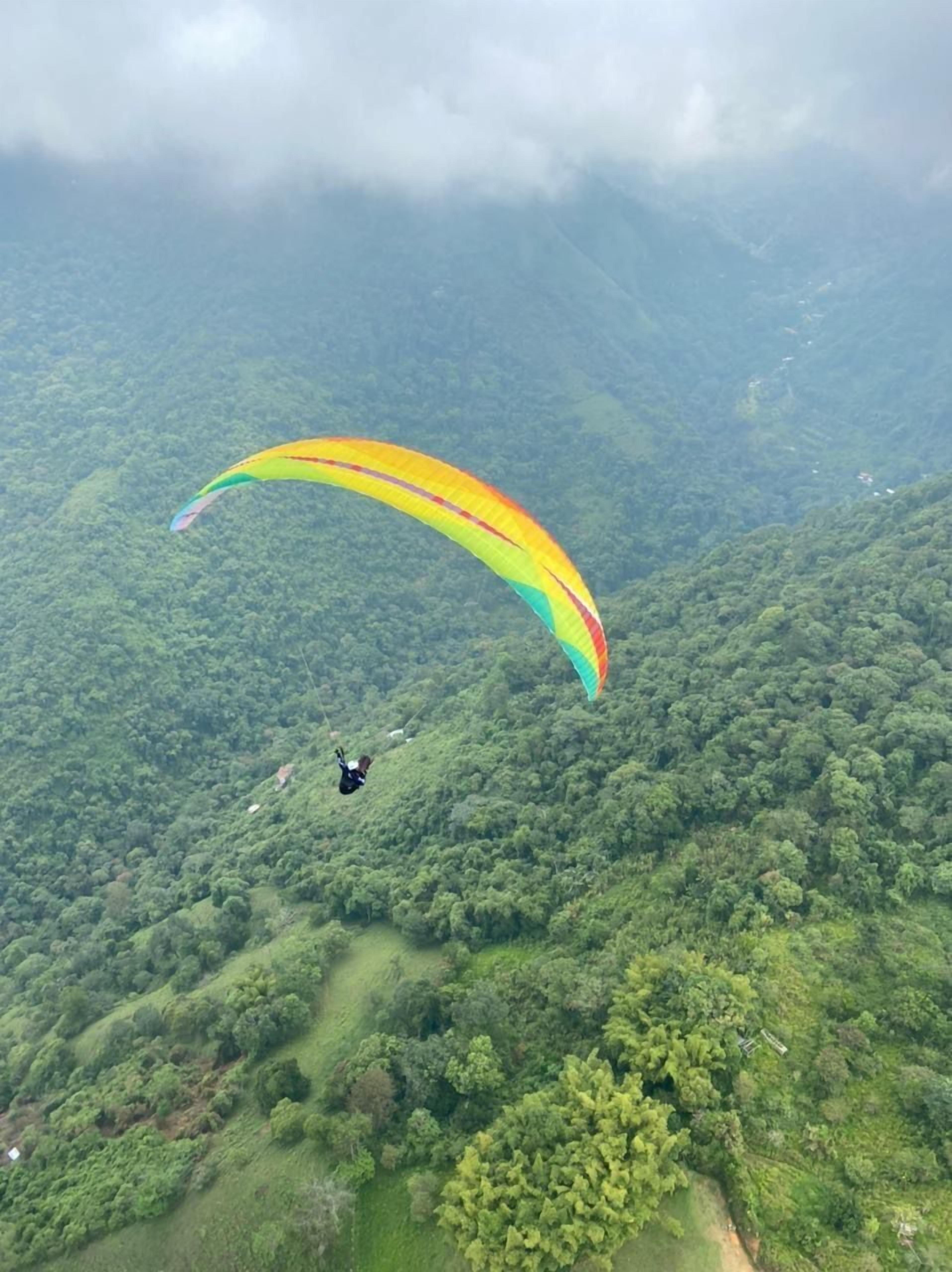 A person paragliding over a lush green landscape with dense vegetation and hills.
