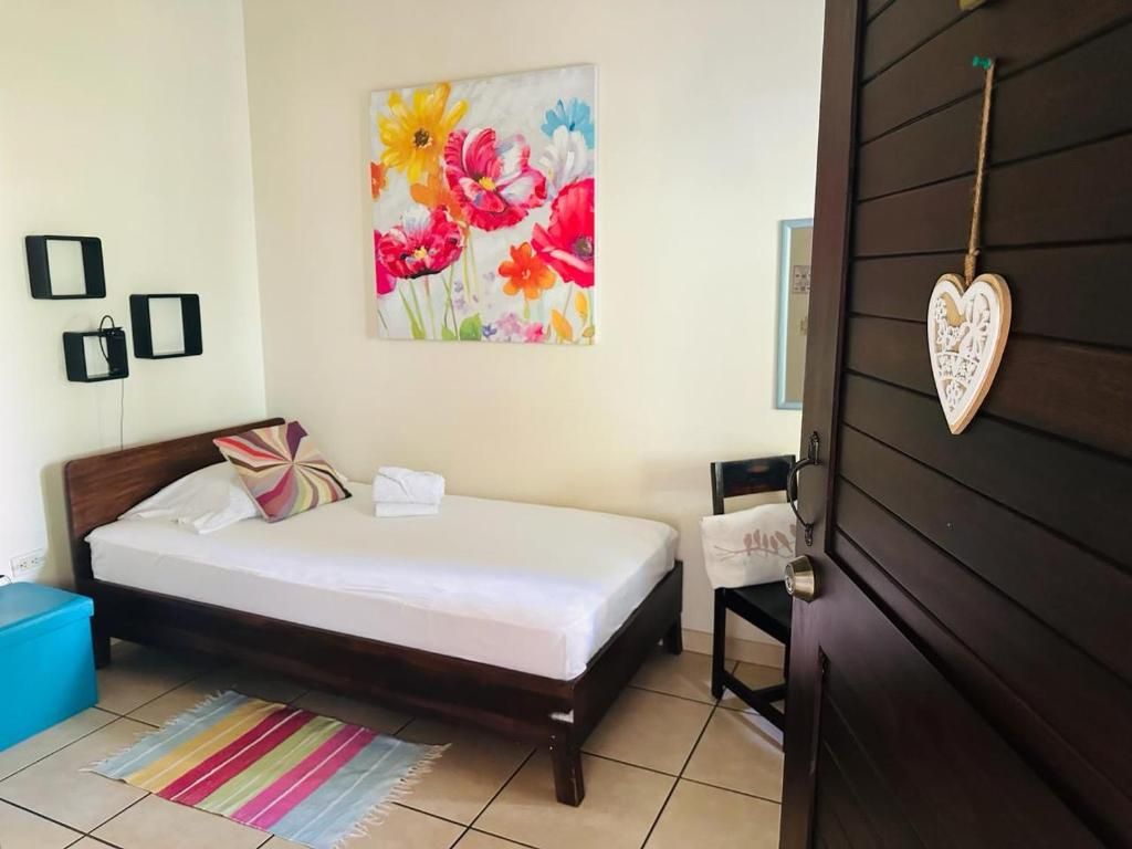 A bedroom with a bed, a colorful rug, a wall with a floral painting, and a heart-shaped decoration.