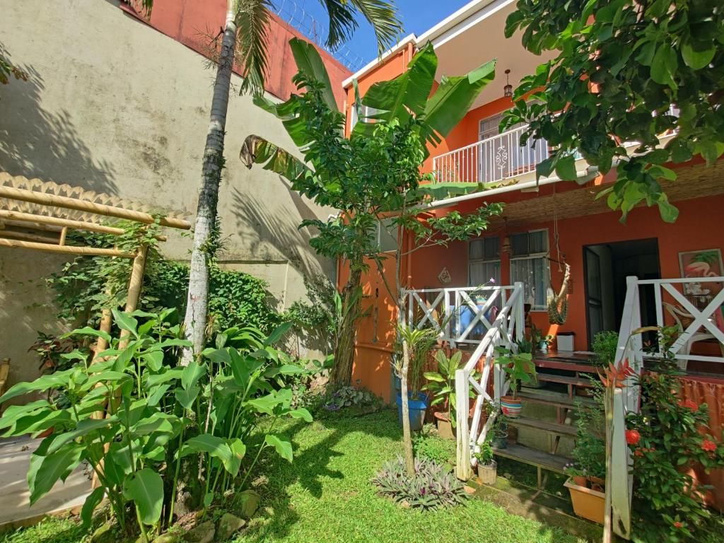 A residential area with a house featuring a balcony, a small garden with various plants, and a white fence.