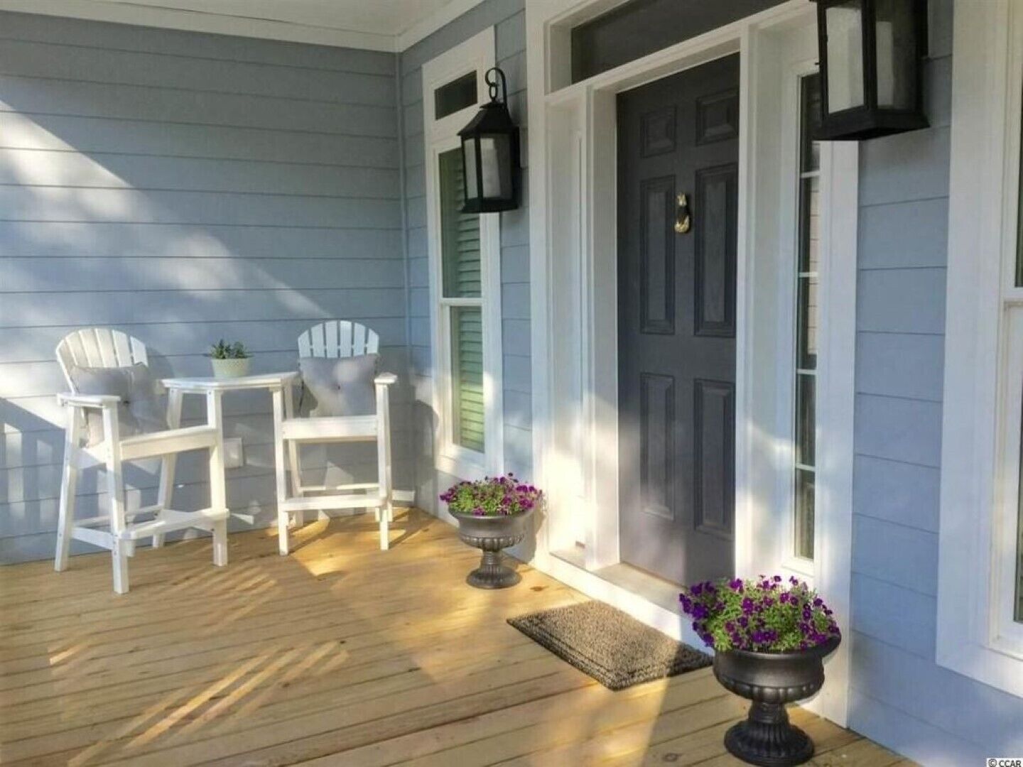 A porch with two Adirondack chairs, a small table, and two flower pots.