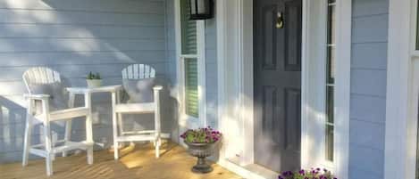 A porch with two Adirondack chairs, a small table, and two flower pots.