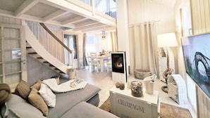 Un espacio habitable amplio con techo alto, chimenea, televisor y una escalera que lleva a un nivel superior.