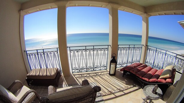 Un balcone con mobili in vimini, un divano decorato e vista sull'oceano.