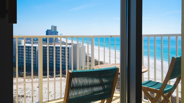 Een balkon met uitzicht op het strand en de oceaan, met twee stoelen en een kleine tafel.