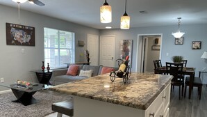 A modern kitchen with a large island, pendant lights, and a dining area with a table and chairs. - Family and Pet friendly  (Pflugerville)
