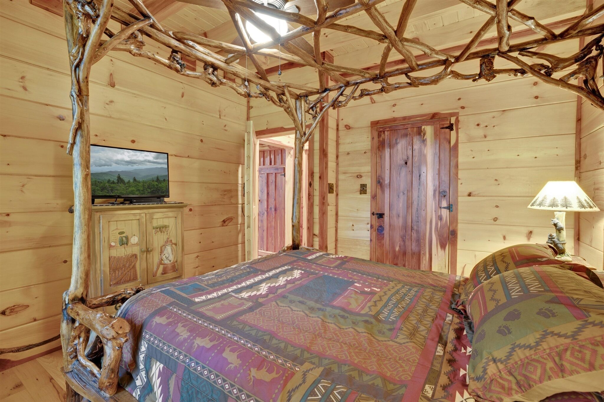 A rustic wooden room with a bed, a television on a cabinet, and a lamp.
