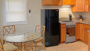 A kitchen with wooden cabinets, a black refrigerator, a stove, and a dining table with chairs.