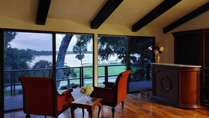 A room with a large window overlooking a lake, two red chairs, a small table with a vase, and a wooden cabinet. - Lake view Chalet  (Mount Dora)