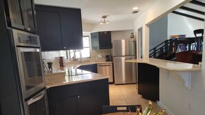 A modern kitchen with dark cabinets, stainless steel appliances, and a wooden dining table with a fruit bowl. - Lake view Chalet  (Mount Dora)