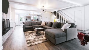 A modern living room with a sectional sofa, a coffee table, and a fireplace. There is a staircase leading to another level. - Hillside Haven (San Diego)