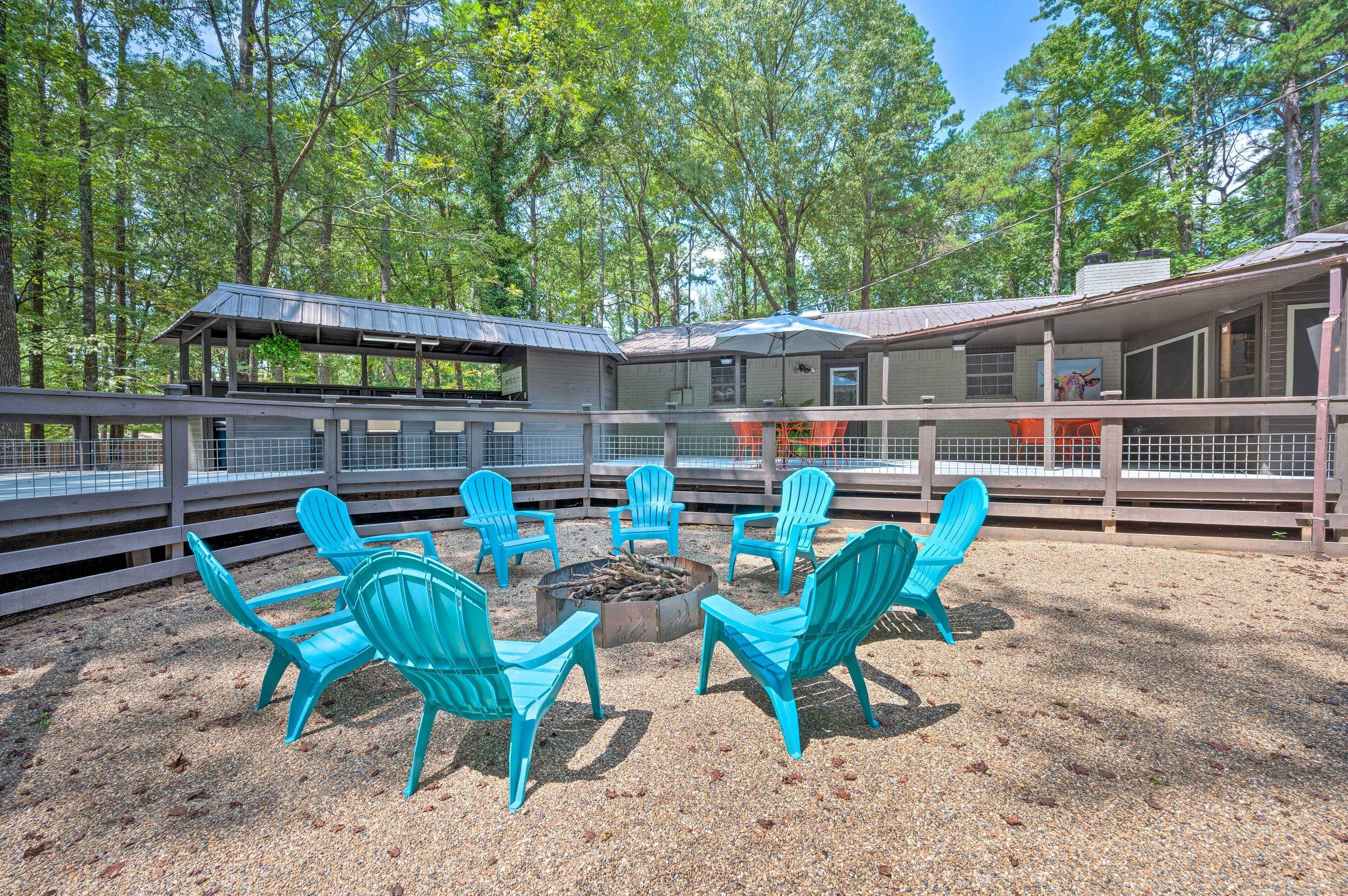 Un espace extérieur aménagé avec des sièges, protégé par un toit, doté de chaises turquoise et d’un foyer, le tout entouré d’une clôture en bois et d’arbres.