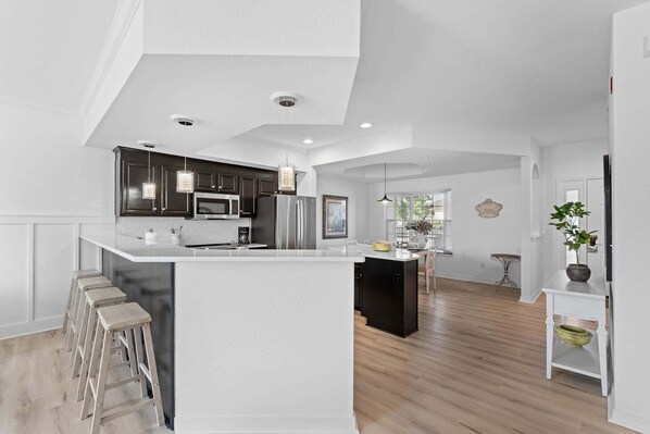 A modern kitchen with a central island, dark cabinets, stainless steel appliances, and a white countertop. - Remodeled Condo • Close to Shows, Shopping & Dining (Branson)