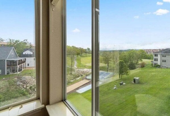 A view from a window overlooking a well-maintained lawn with a small pond and a golf course in the distance.