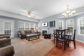A living room with a fireplace, a dining area with a table and chairs, and a ceiling fan. - Central Branson Townhome | Patio | Pool | Sleeps 8 (Branson)