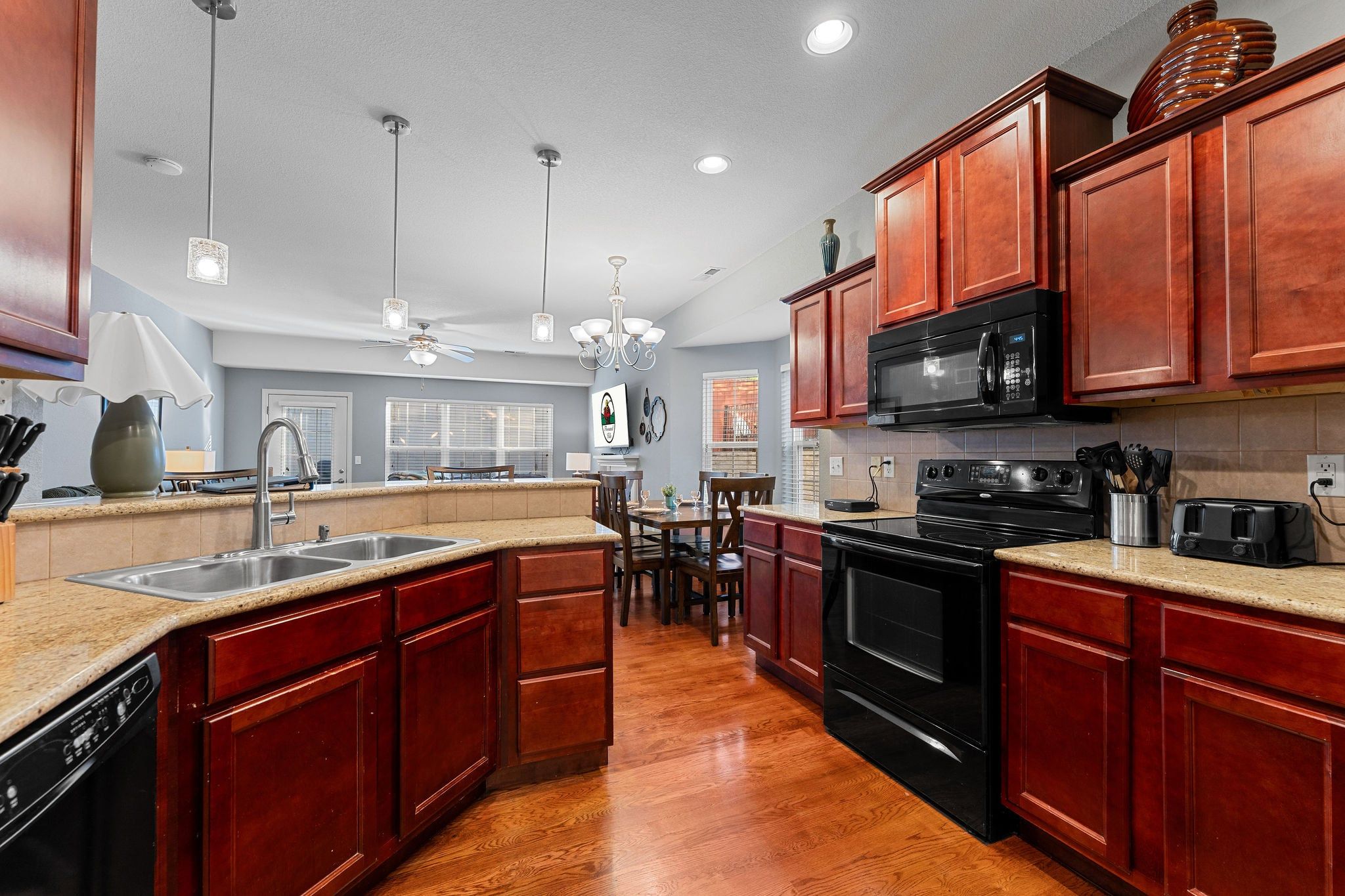 A kitchen with wooden cabinets, a black microwave, a stove, and a sink.