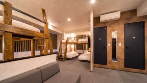 Una habitación con literas, un sofá y un escritorio. Hay dos puertas y un equipo de aire acondicionado en la pared.