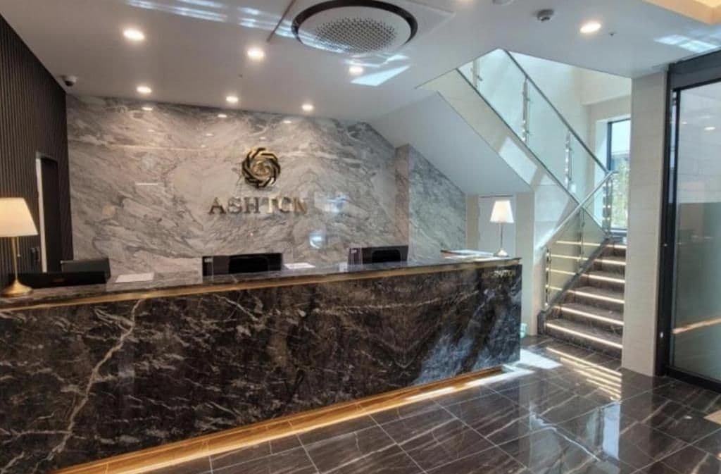 A reception desk with a marble countertop and a logo, a staircase, and a modern interior design.