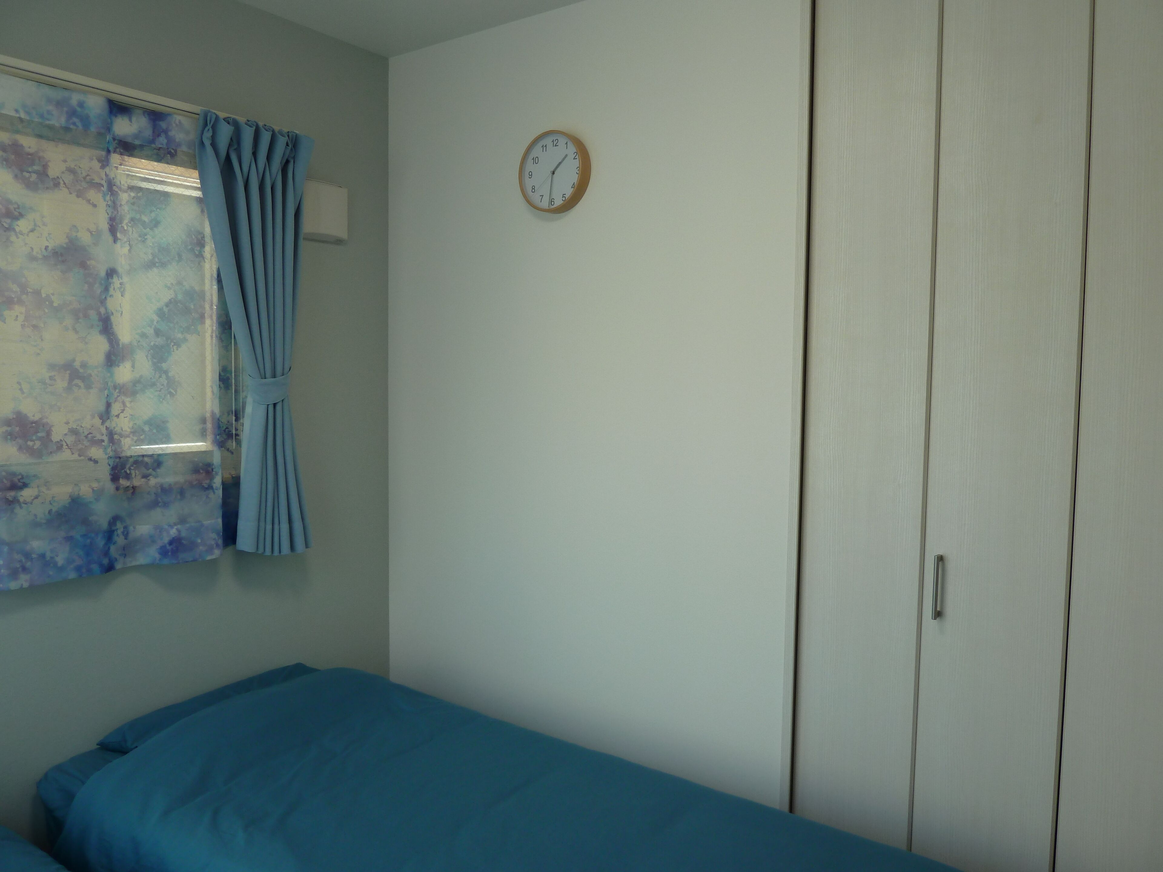 A bedroom with a bed, a wardrobe, a clock, and a window with curtains.
